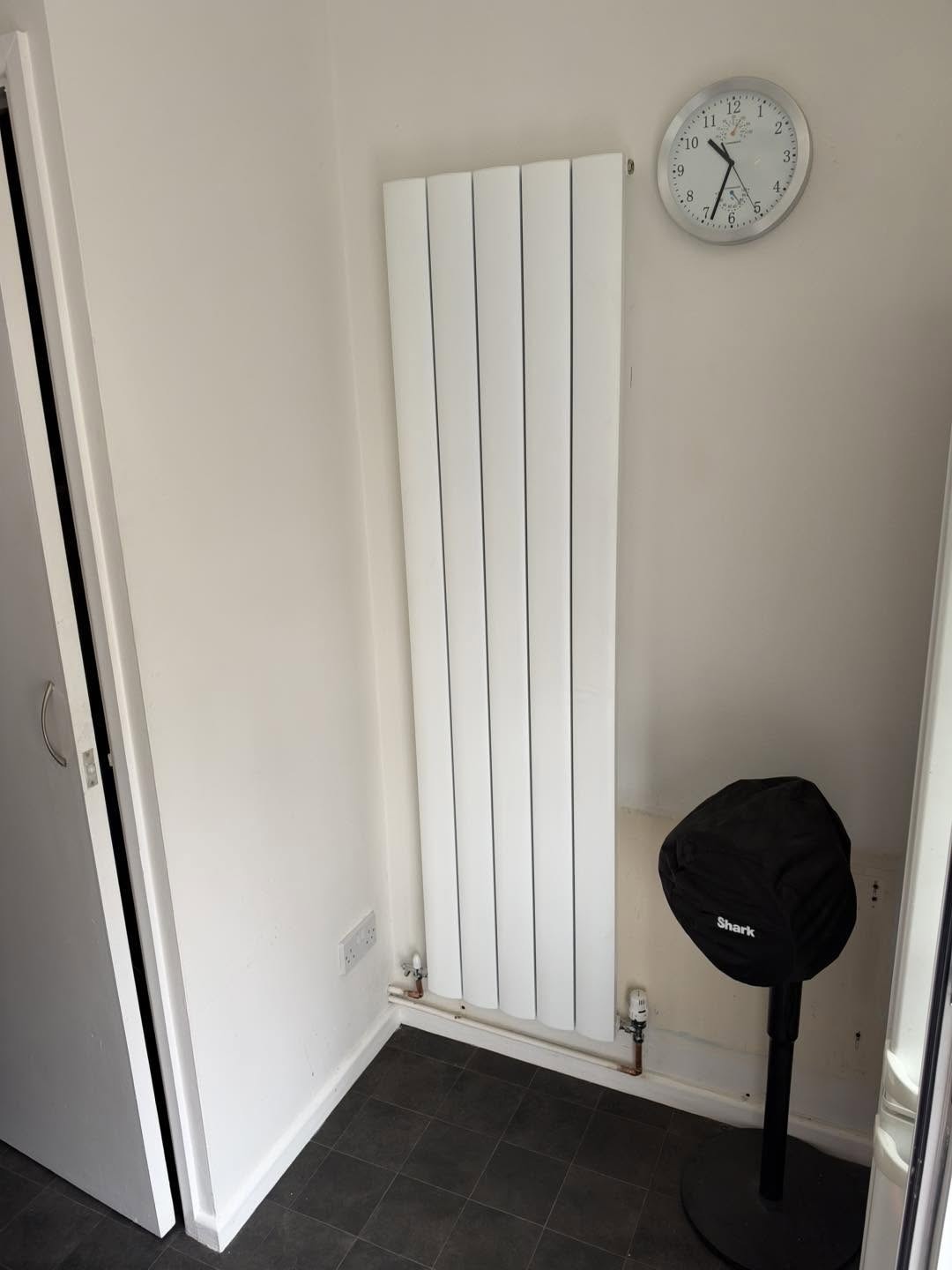 A tall white vertical designer radiator fitted in a hallway
