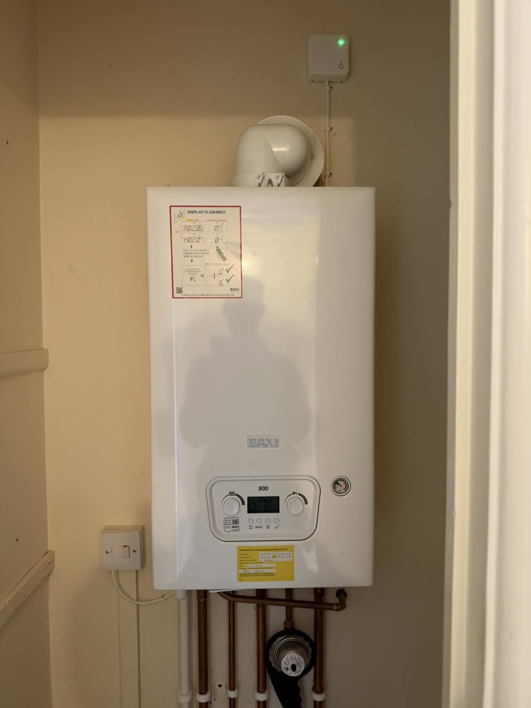 White combi boiler fitted in an alcove with pipework below