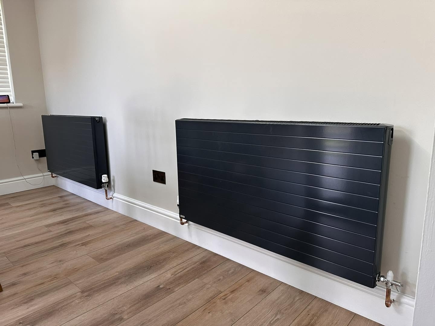 Two anthracite horizontal designer radiators on a light wall above a wood floor