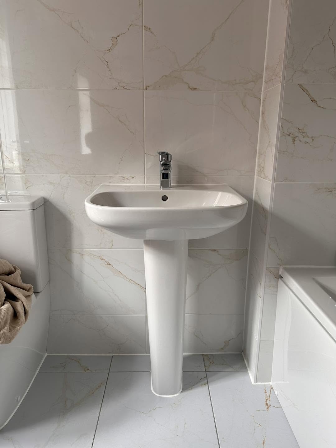 White pedestal basin with a chrome mixer tap and marble effect tiles