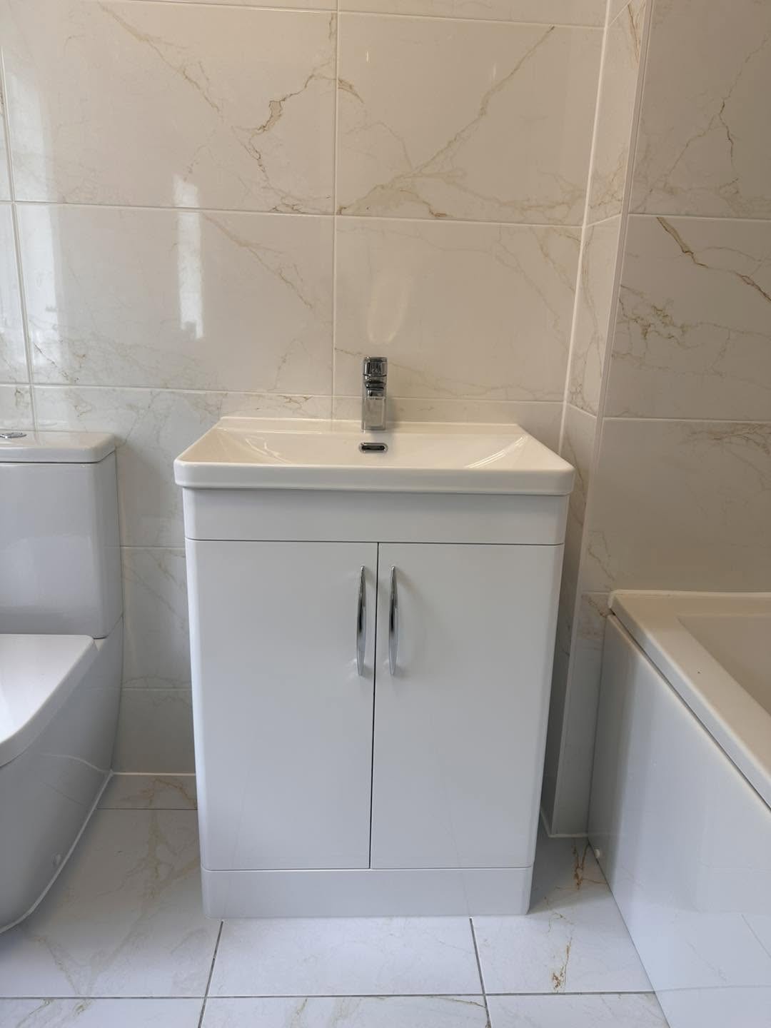 White vanity basin unit beside a bath with marble effect tiles