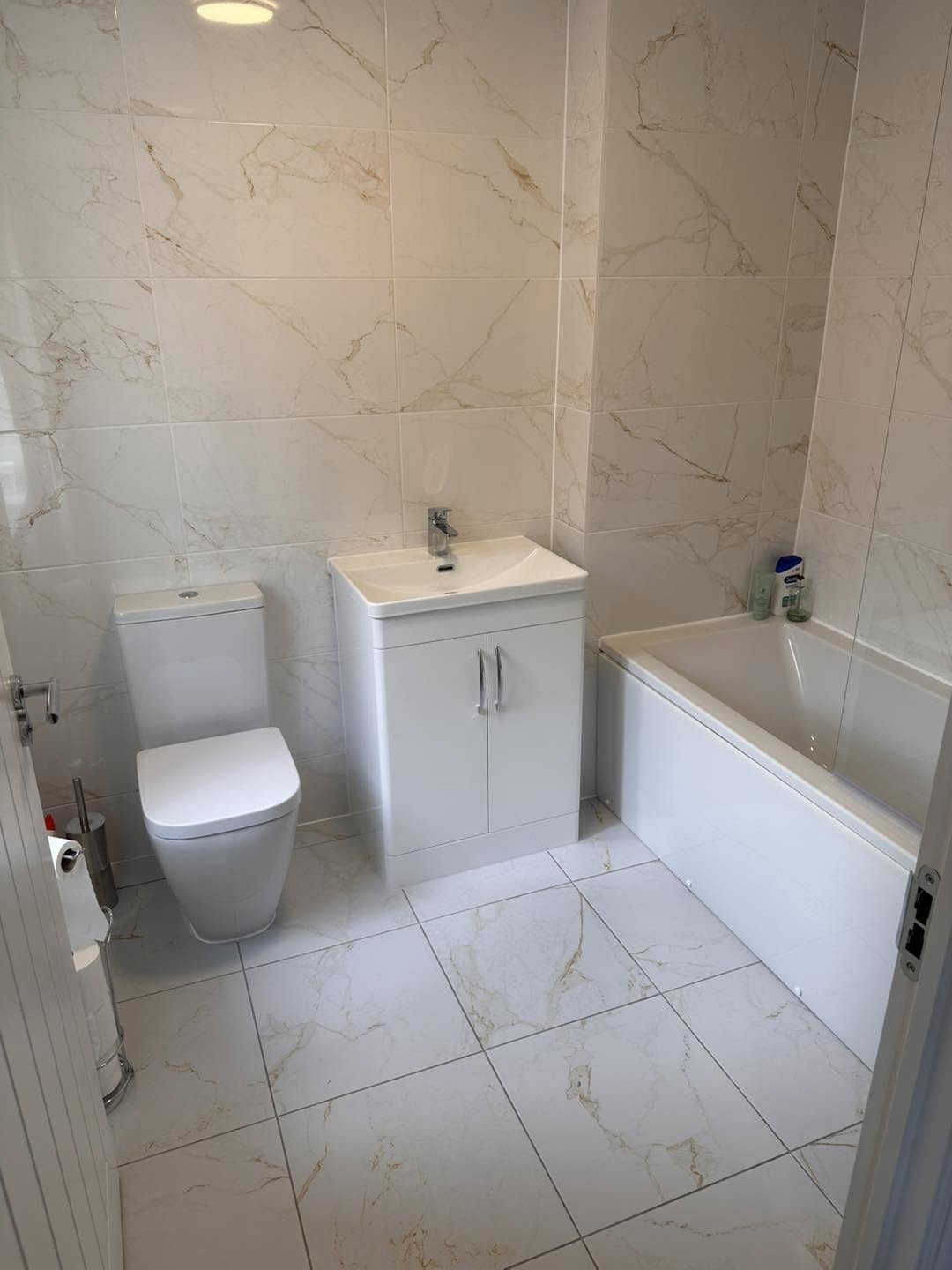 Bathroom with toilet, vanity unit and bath on a marble effect tiled floor