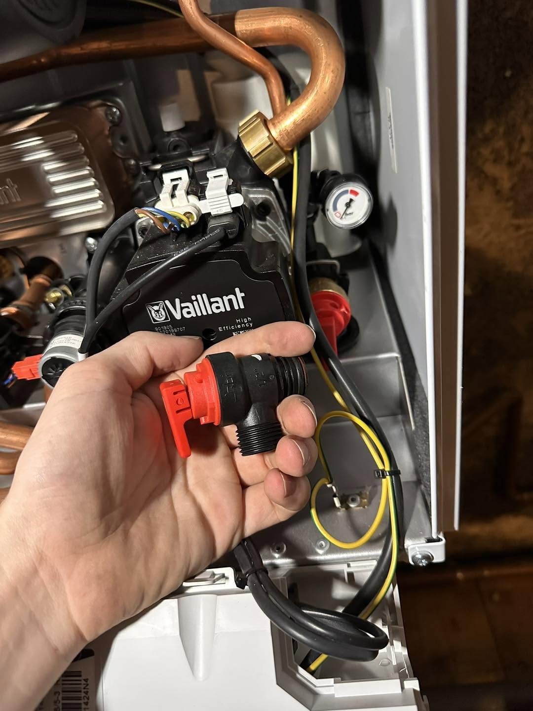 Hand holding a Vaillant boiler part beside the open boiler