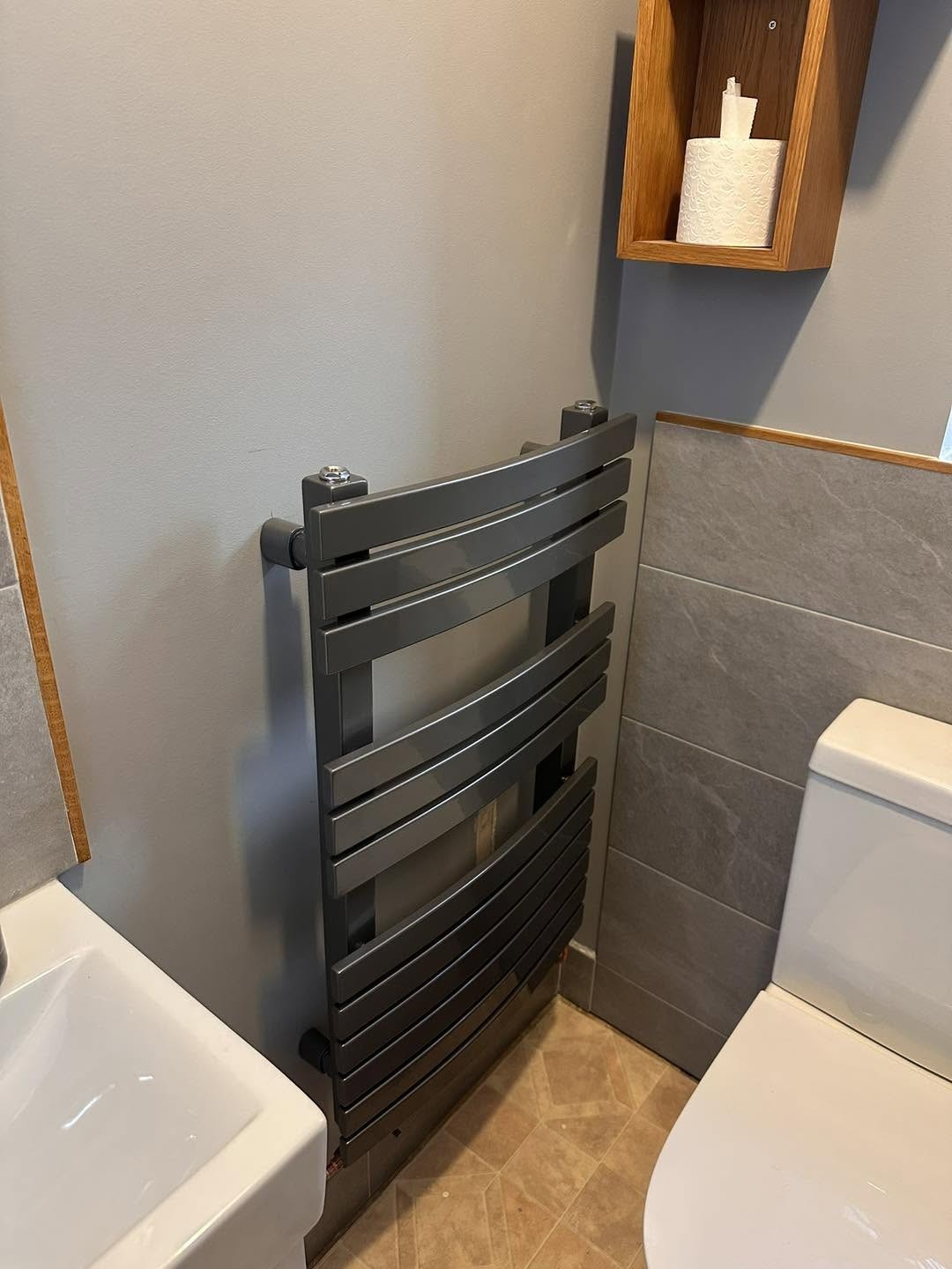 Anthracite curved towel radiator beside a toilet with grey tiles