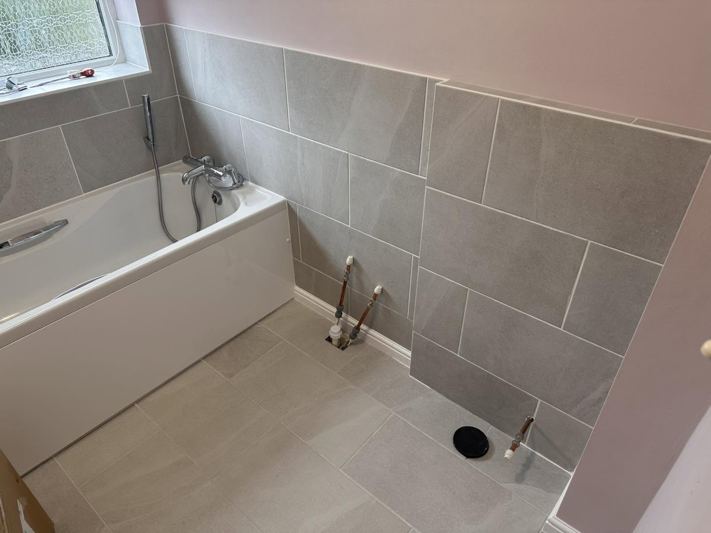 Bath with a white panel and large grey wall tiles
