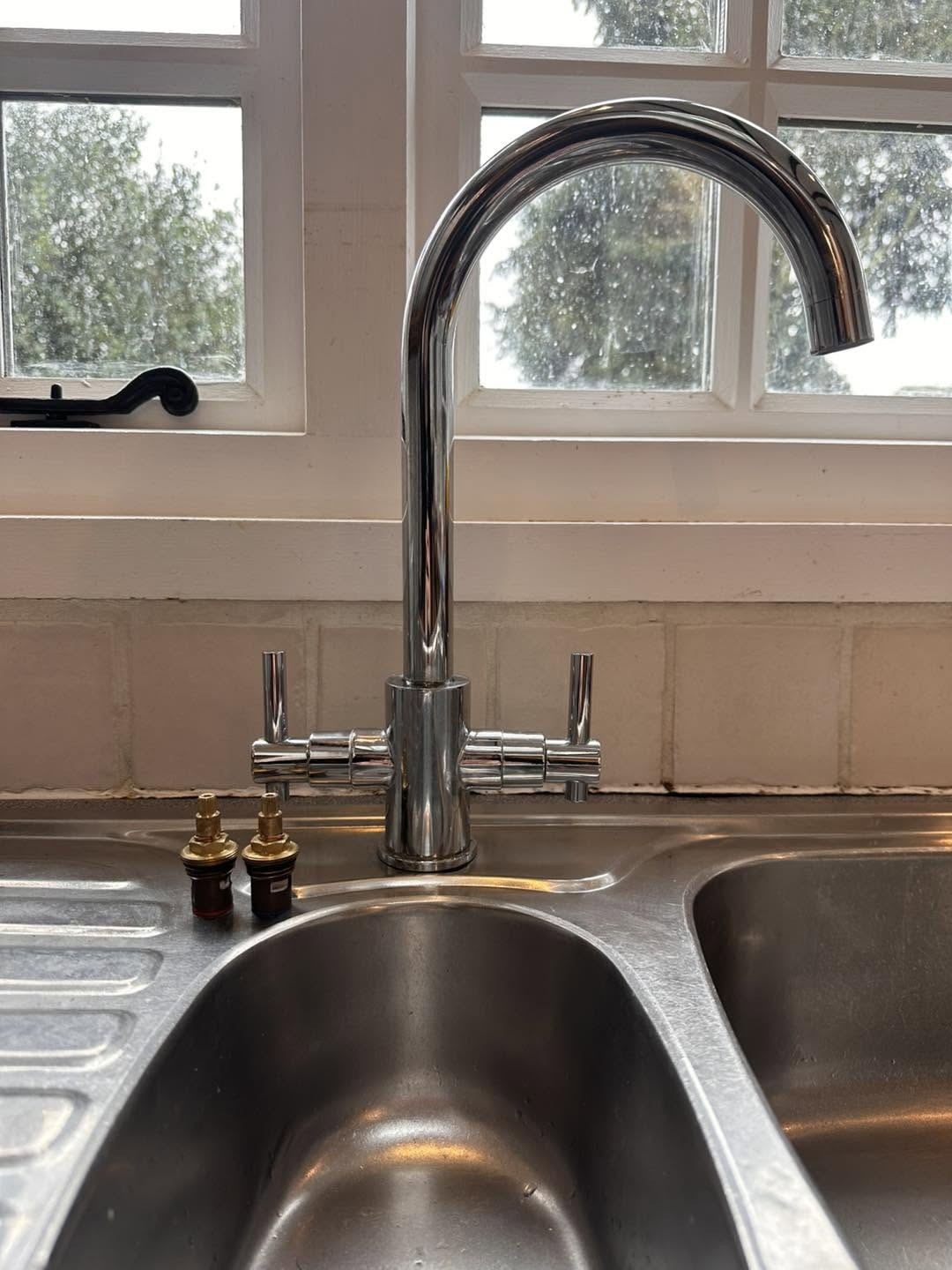 A chrome swan neck kitchen mixer tap over a stainless steel sink