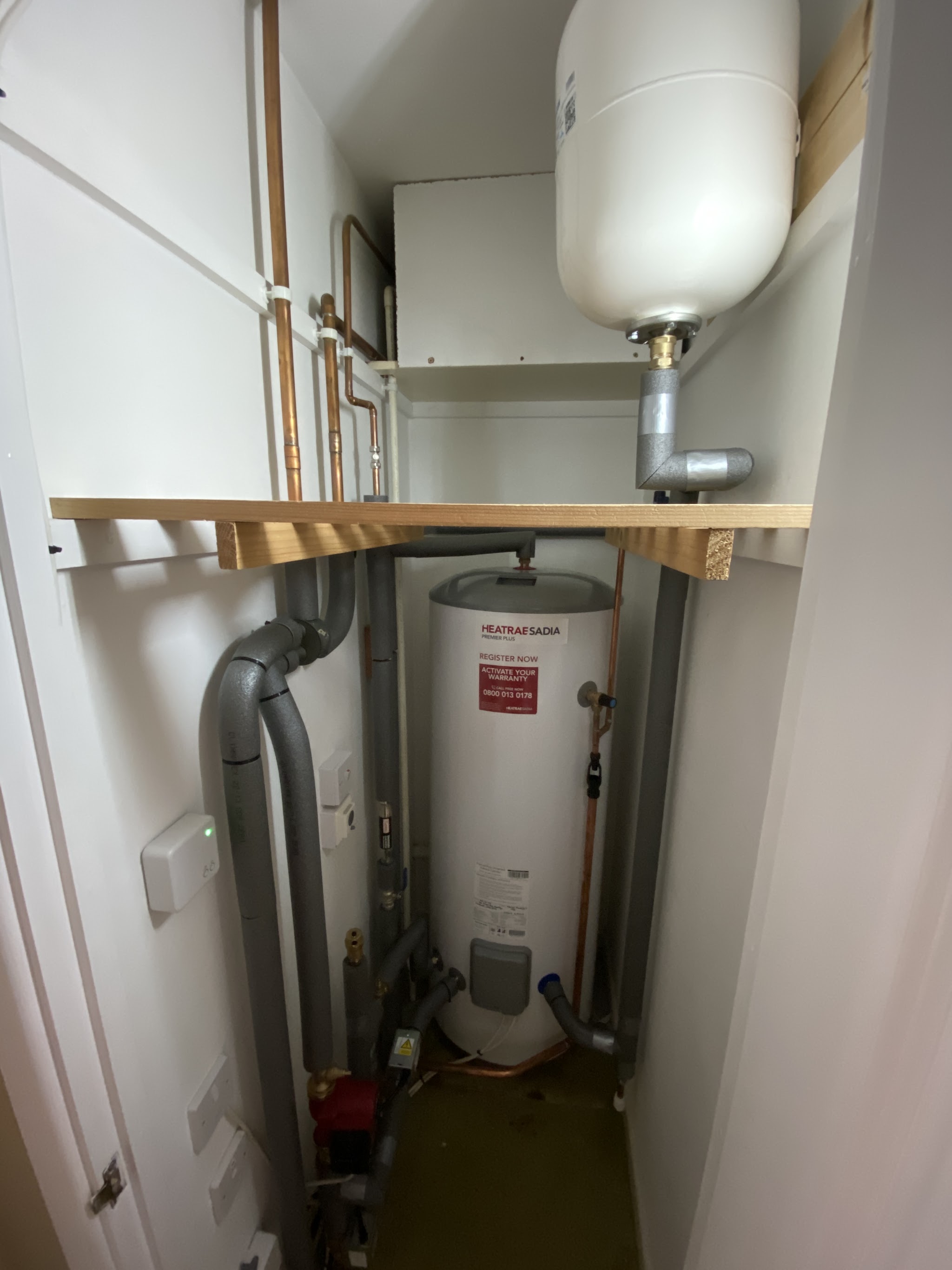 A replacement hot water cylinder in an airing cupboard with the expansion vessel on a shelf above