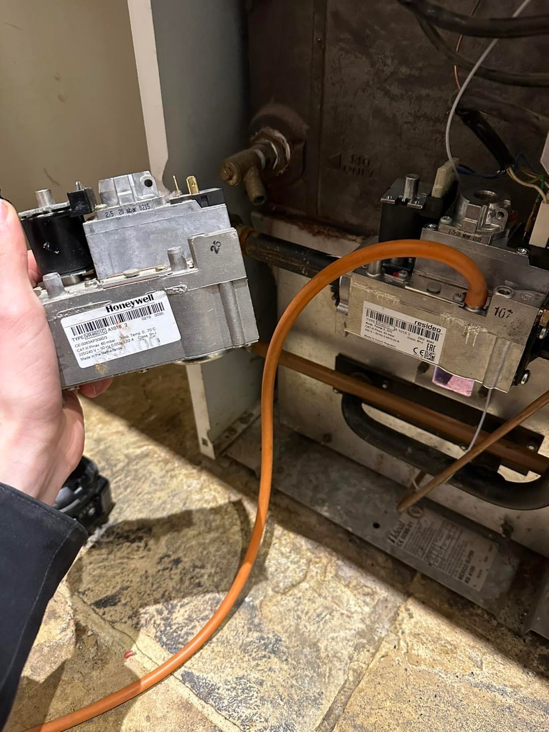 Hand holding a Honeywell gas valve beside an old floor standing boiler under repair
