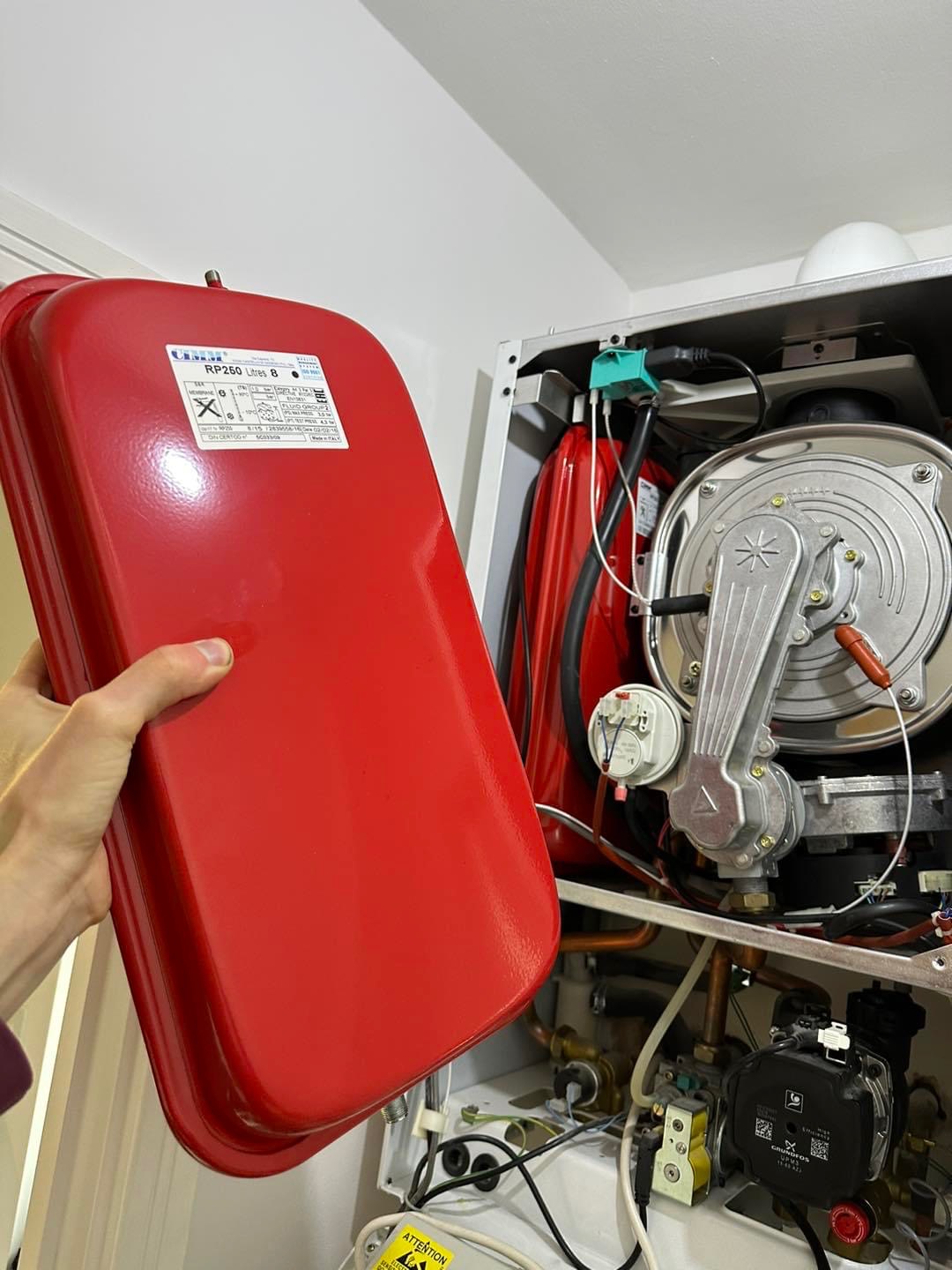 Hand holding a red expansion vessel beside an open boiler