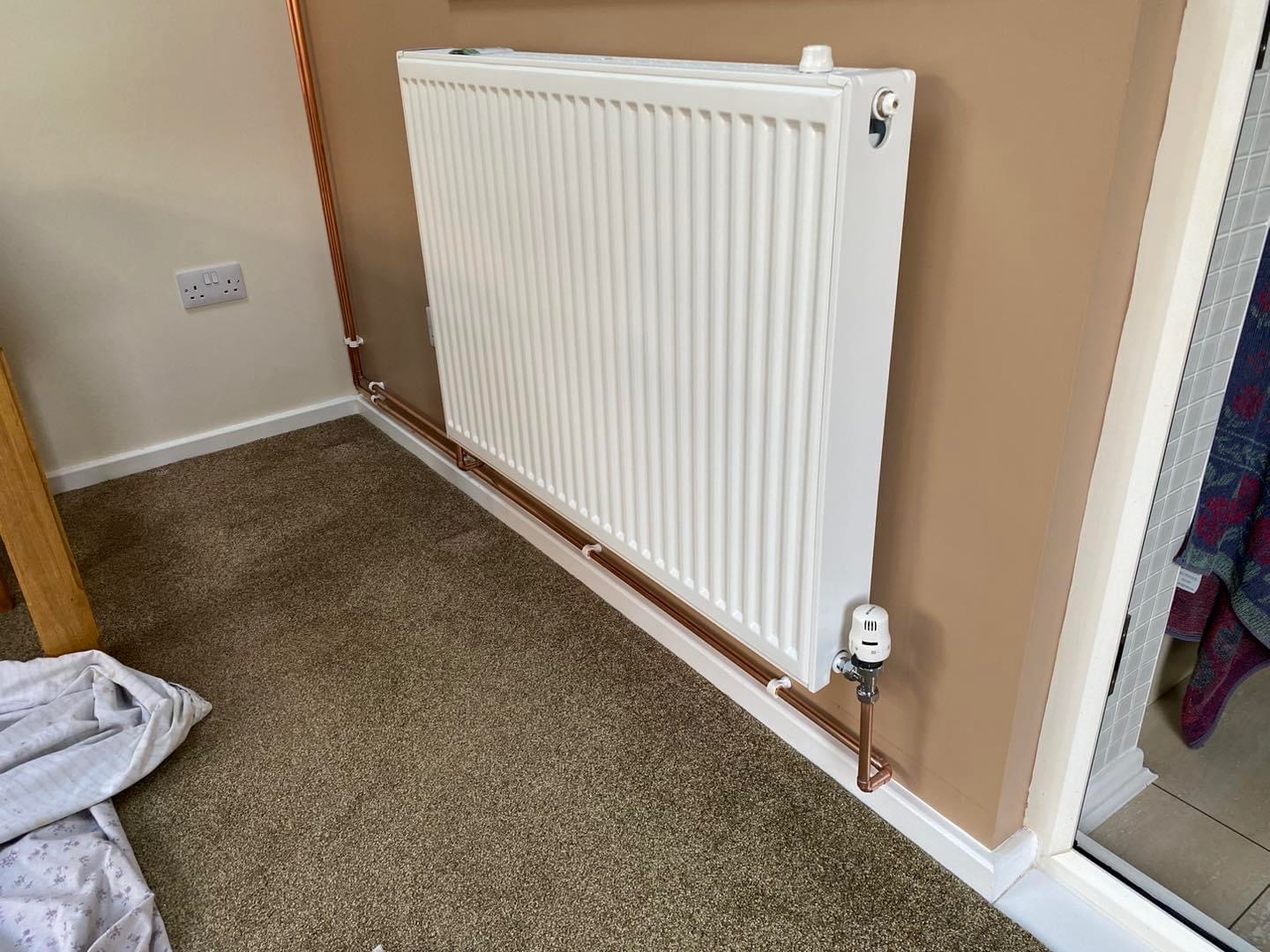 Newly fitted white double panel radiator with a thermostatic valve and new copper pipe along the skirting